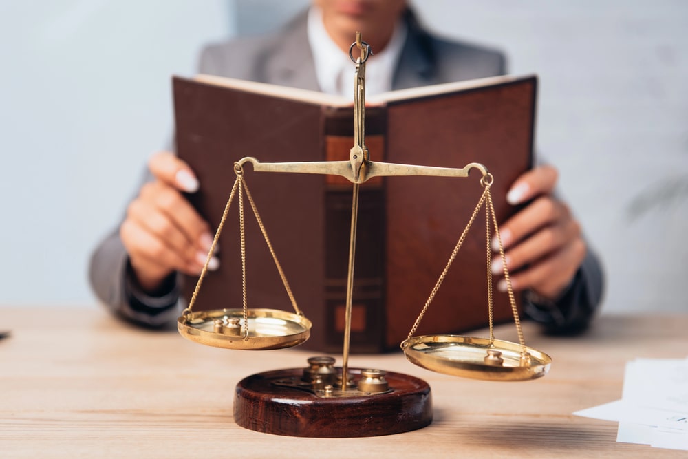 Scales of justice on desk with attorney reading law book, symbolizing personal injury law in Bloomfield NJ.