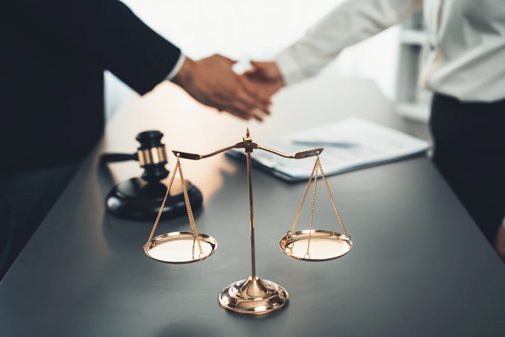 Scales of justice and gavel on desk with lawyer and client shaking hands, representing personal injury law in Orange NJ