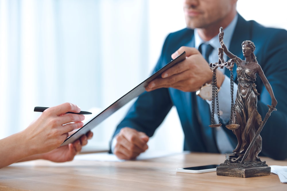 Lawyer in suit handing legal documents to client beside Lady Justice statue, symbolizing legal help in Perth Amboy, NJ.